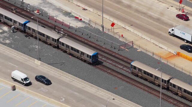 High angle of urban transit showing cars driving along a highway next to a Chicago L Train moving along railway tracks during daytime commute