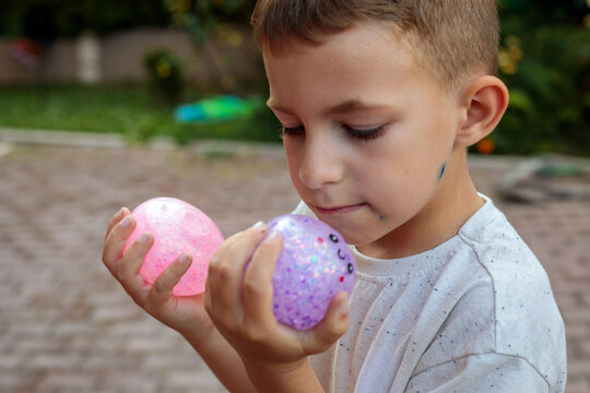 Smiling little boy playing with a glittery dumpling shaped squishy toy outdoors, squeezing a colorful sensory stress relief toy during fun playtime in the garden