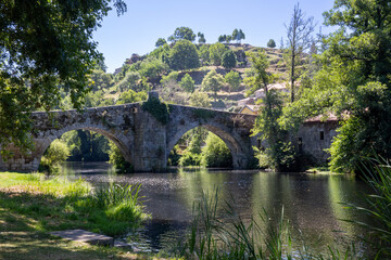 Fototapeta premium Historic Romanesque Vilanova stone bridge over the Arnoya river in Allariz, Ourense, Galicia, Spain. Ancient medieval architecture landscape on a sunny summer day.