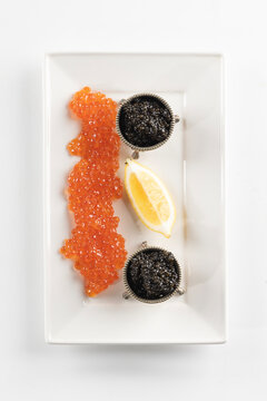 Red and black caviar on a white platter. Natural omega. A slice of lemon next to the caviar. Luxury gourmet food. Isolated object. Natural omega. An exquisite snack. Isolated object. Top view