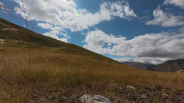 4K timelapse video of white clouds passing fast over a beautiful golden grass hill under blue sunny sky.