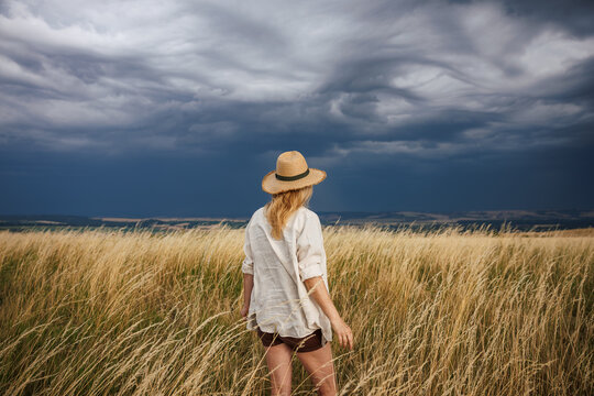Weather in summer. Woman with straw hat anticipating storm and watching dramatic clouds over countryside