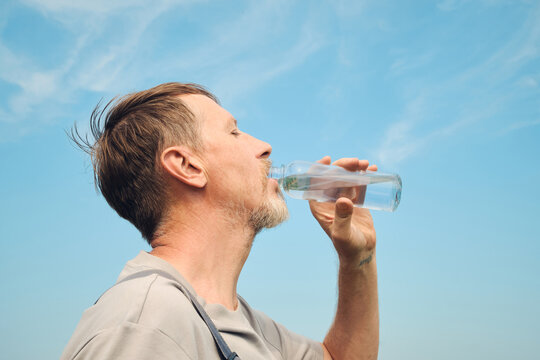 Mature man drinking refreshing water from glass bottle on sunny day