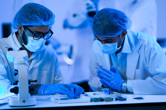 Laboratory colleagues study a test sample during research in a dramatic blue-lit laboratory while wearing white lab coats and blue protective gloves and modern scientific (No. 3983).