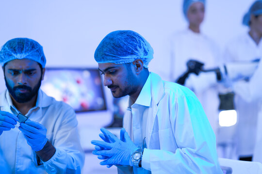 Masked researchers concentrate on a delicate sample in a moody high-technology lab while wearing white lab coats and blue protective gloves and modern scientific innovation (No. 4053).
