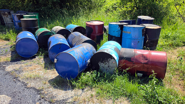 Ecological hazard of discarded industrial oil drums polluting a green roadside field