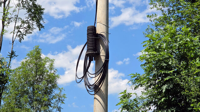 Fiber optic splice closure with coiled black cables mounted on a concrete utility pole