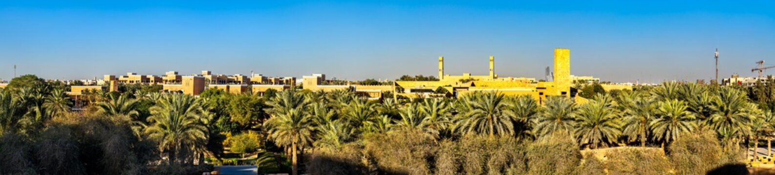Panoramic view of the historic mud brick architecture of At Turaif district in Diriyah surrounded by lush palm trees under a clear blue sky