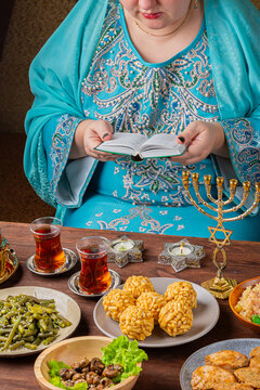 A Jewish woman prays from the siddur at a table set out with food