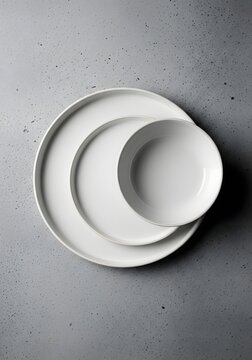 Minimalist white ceramic plates and a bowl on a textured grey concrete background view