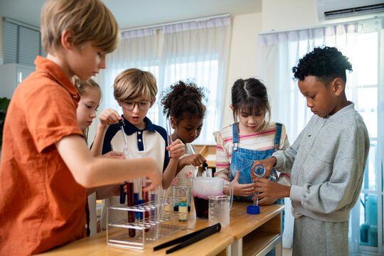 Multiethnic group of elementary students collaborating on a colorful chemistry science experiment. Schoolchildren working together, pouring liquids and using test tubes during STEM laboratory lesson.