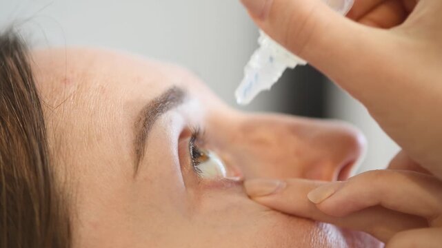 Close up woman applying clear eye drops indoor natural light soft background care routine