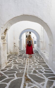 White archways between houses, Young woman with red dress in the old town of Lefkes, Paros, Cyclades, Greece