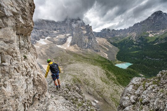 Young man, mountaineer on a fixed rope route, Via Ferrata Vandelli, view of Lago di Sorapis, Sorapiss circuit, mountains with low clouds, Dolomites, Belluno, Italy