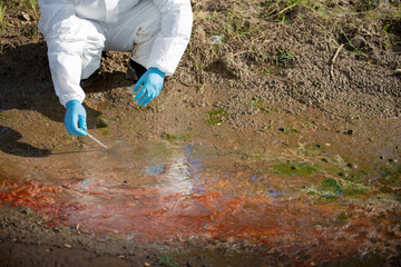 Ecologist analyzing contaminated water source with flask and tools in protective gear on polluted soil © nikomsolftwaer