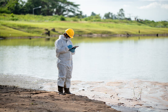 Environmental scientist in protective clothing examining water quality using a flask by a peaceful lake setting
