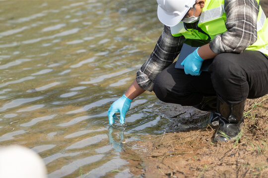 Ecologist examining water sample with flask by riverbank in protective gear for environmental research and analysis