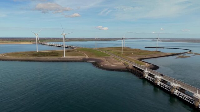 Aerial wide angle shot of a long concrete breakwater pier stretching into the calm green sea with a red and white lighthouse at the end on a bright sunny day