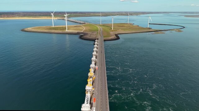 Aerial high angle view of a massive storm surge barrier and road dam with wind turbines on an artificial island separating the sea and estuary on a sunny day