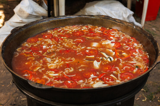 Traditional fish soup with fresh tomatoes being cooked outdoors at a vibrant culinary food festival