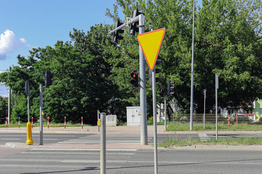Yield sign stands at urban intersection. Traffic lights control vehicles and pedestrians. Road safety background covers city traffic rules. Street crossing marks public transport infrastructure.