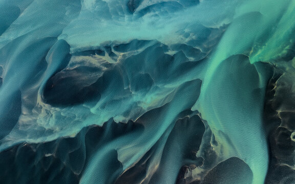 Aerial view of glacial river patterns with turquoise sediment and dark volcanic sand in Iceland.