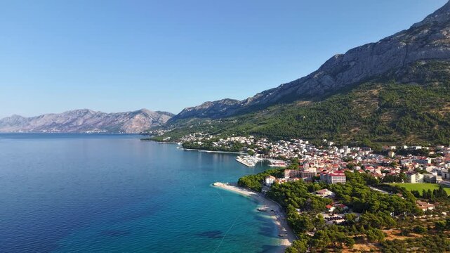 Aerial view of the coastal town of Brela on the Makarska Riviera in Croatia, featuring turquoise Adriatic sea, pebble beaches, and Biokovo mountains