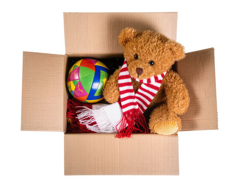 Isolated fluffy brown teddy bear wearing scarf with colorful ball inside open cardboard box ready for delivery.