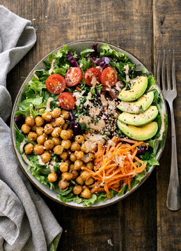 Healthy fresh salad bowl with chickpeas, avocado, and cherry tomatoes on a rustic table