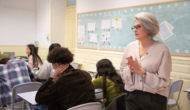Senior teacher clapping hands, engaging with multi-ethnic students learning in a classroom