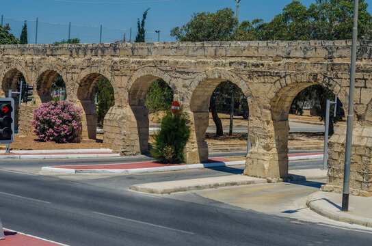 Ancient 17th-century Wignacourt Aqueduct limestone arches contrast beautifully with modern asphalt roads and traffic lights in sunny Malta.