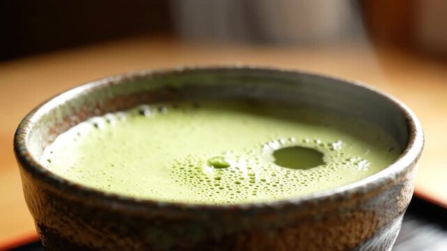 Close-up of bamboo whisk frothing bright green matcha tea in a traditional ceramic bowl
