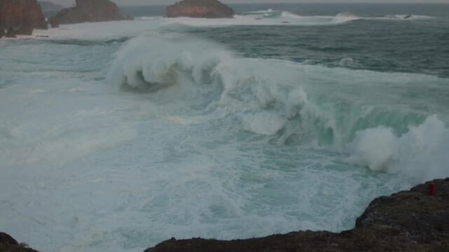 Powerful Ocean Waves Crashing Against Rocky Coastline with Foam and Distant Cliffs at Stormy Sea