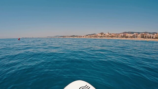 V&iacute;deo de paddle surf grabado en primera persona desde la tabla, avanzando sobre el mar en calma frente a la costa de El Masnou. Se ve el horizonte mediterr&aacute;neo, agua azul, una se&ntilde;al mar&iacute;tima en la dis