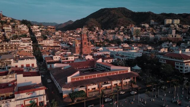 Drone orbital sunset footage of Parroquia Nuestra Senora de Guadalupe church showcasing architectural tower against warm magenta light with coastal city backdrop