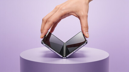 Hand folding a modern foldable smartphone on a pedestal in a minimalist studio with a purple background. © Curioso.Photography