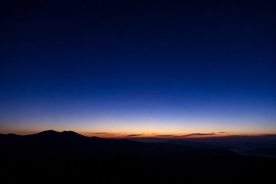 The dark horizon before dawn, a faint sliver of pale light emerging, signaling the imminent sunrise.
