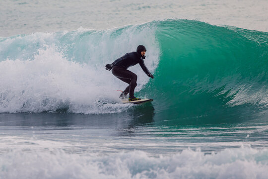 Surfer in wetsuit riding on glassy wave in ocean. Winter surfing