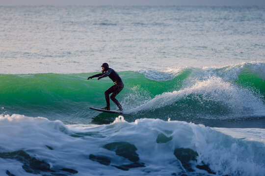 Surfer male riding on glassy wave in ocean with evening sunlight