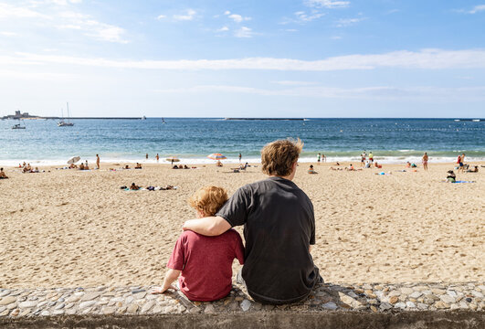 Two Brothers Sit on a Bench in Front of a Beach