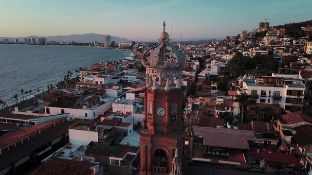 Drone orbital sunset footage of Parroquia Nuestra Senora de Guadalupe church showcasing architectural tower against warm magenta light with coastal city backdrop