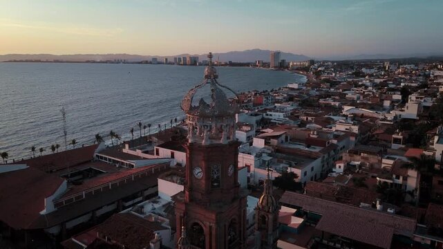 Drone orbital sunset footage of Parroquia Nuestra Senora de Guadalupe church showcasing architectural tower against warm magenta light with coastal city backdrop