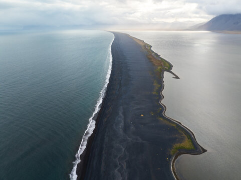 Aerial view of the long black sand spit at Hvalnes with crashing waves and calm water on either side in Sveitarfelagid Hornafjordur, Iceland.