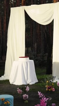 Vertical video. White fabric wedding arch with a round cake and floral decor in a pine forest venue.