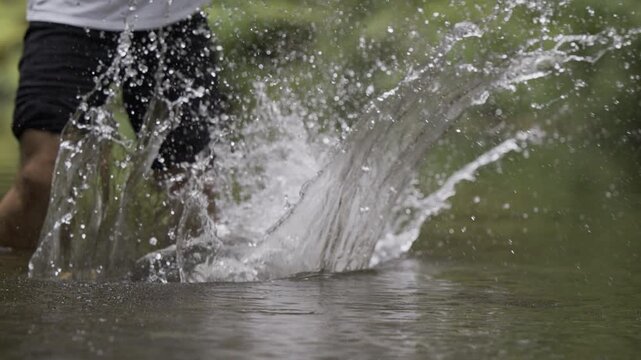 Man using large board to cut through shallow water and make splashes - low, closeup, slow motion shot