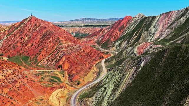 Winding road curving through colorful Danxia landform mountains under clear blue sky in Xinjiang, China.