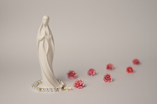 Virgin Mary statue with rosary beads and pink flowers on light background, Christian faith concept with copy space
