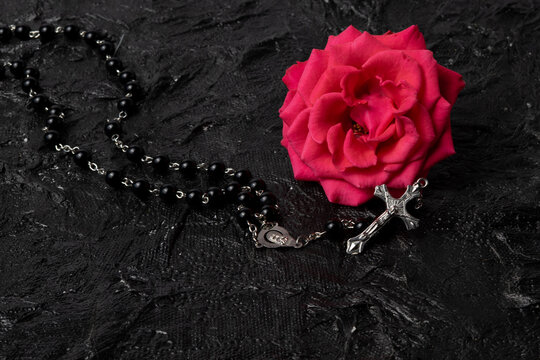 Rosary beads with pink rose flower on black textured background, Christian prayer and faith concept with copy space