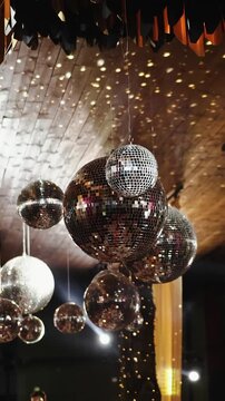 Vertical video. Mirror disco balls hanging from the ceiling with sparkling reflections at a wedding venue.