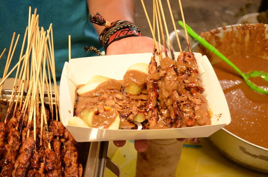 Indonesian satay and braised egg dish served in a takeaway box with rich peanut sauce, authentic street food photography.